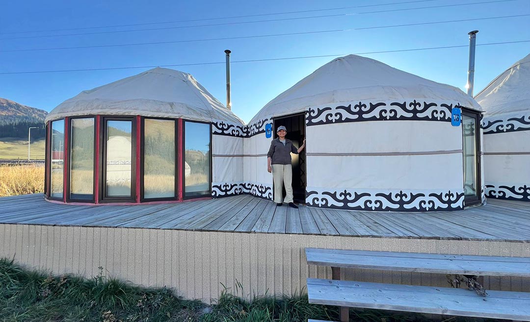 Sofia Shamsunahar's mother standing outside a traditional nomadic yurt during a cultural tour with Ak-Sai Travel in Kyrgyzstan.
