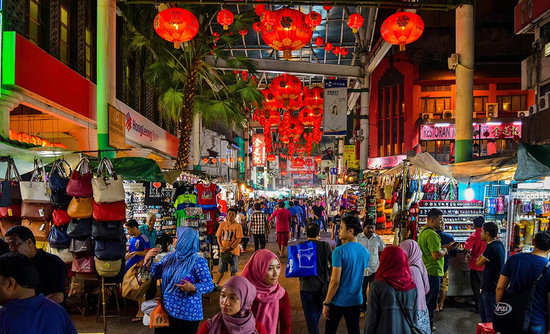 A crowded Petaling Street in KL Chinatown with red Chinese lanterns and shoppers, representing high-traffic areas during the 2026 festive travel season in Malaysia.