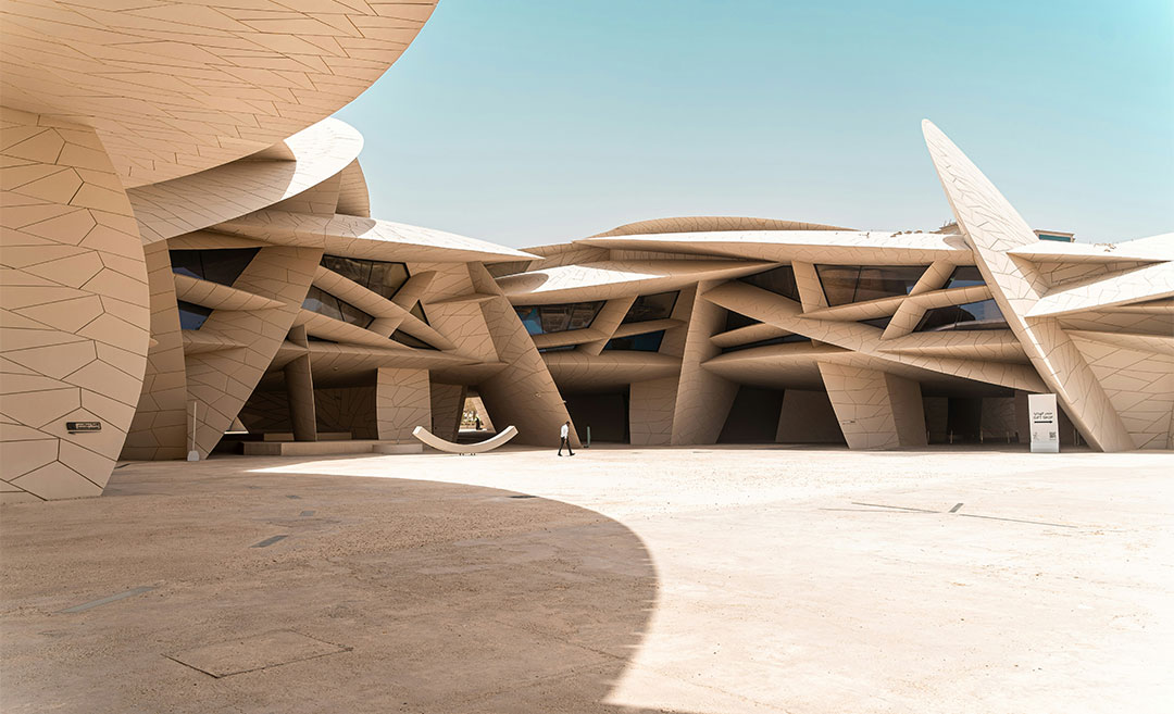The National Museum of Qatar in Doha, featuring iconic desert rose-inspired architecture with a person walking toward the entrance.
