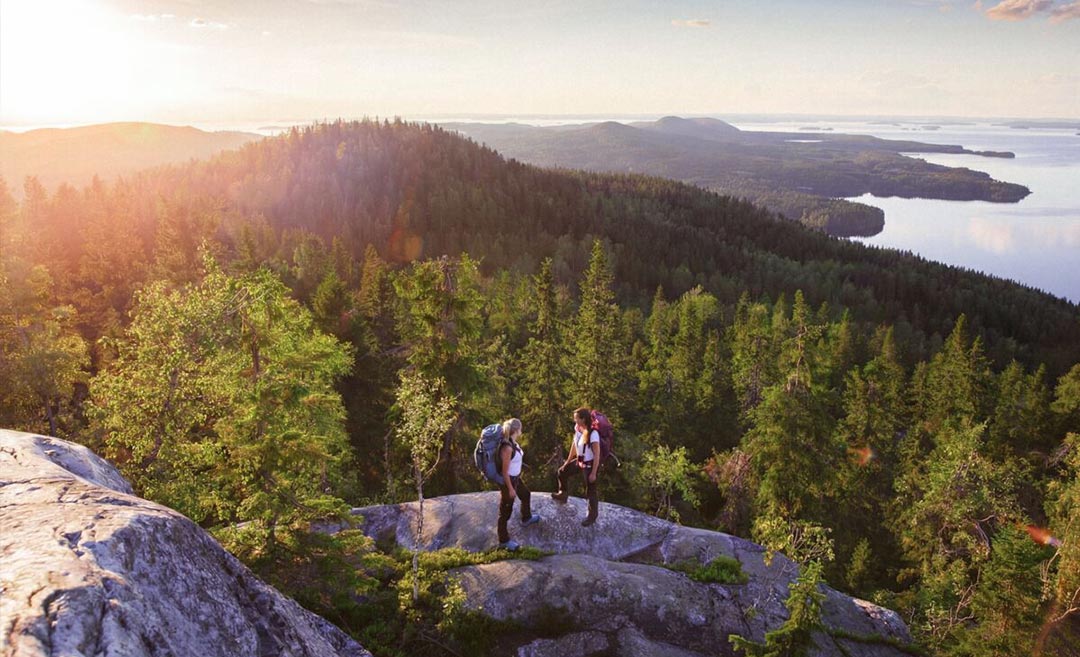 Aerial drone view of two female hikers standing on the rocky summit of Koli Hill overlooking the forests and lakes of Finland.