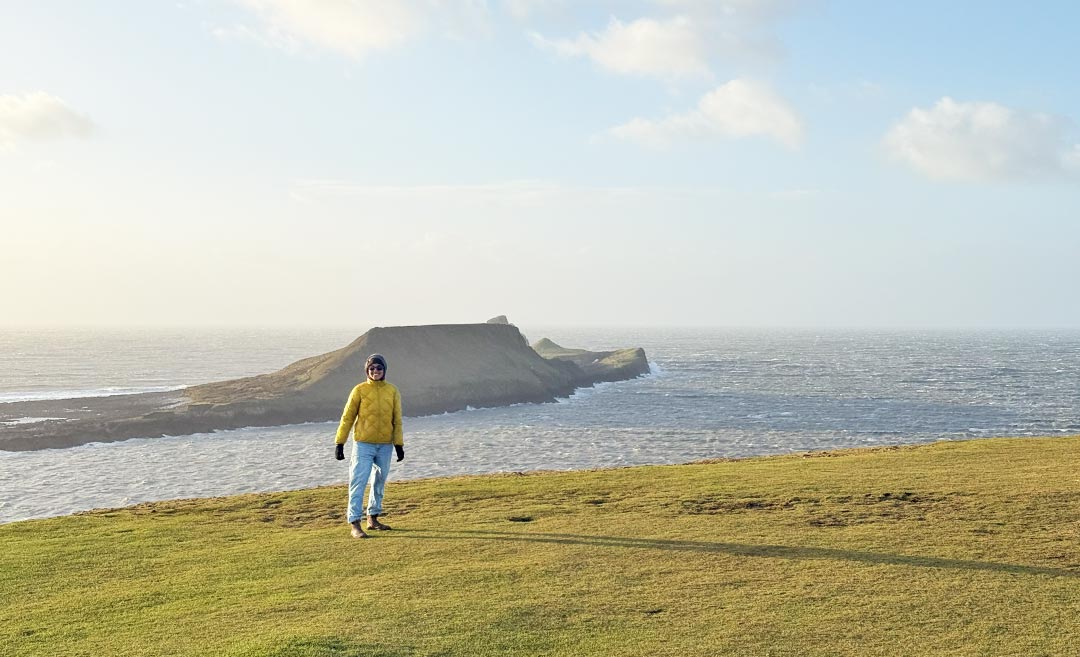 A dramatic view of Worm’s Head at Rhossili Bay, South Wales, on a windy day with waves crashing against the tidal island.