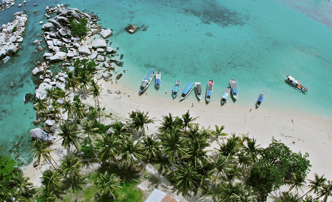 A panoramic drone view of Lengkuas Island in Belitung, Indonesia, featuring its white sand beaches and clear turquoise water.