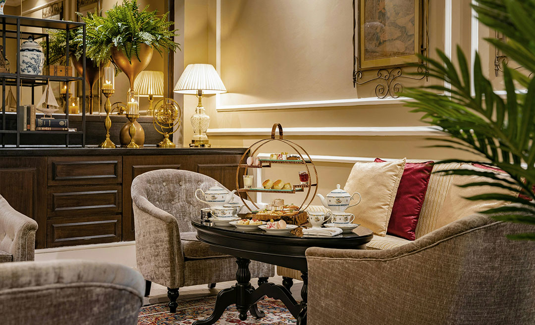 A classic afternoon tea set with a tiered tray of savouries and sweets on a table between two elegant single-seater sofas at The Majestic Hotel Kuala Lumpur.
