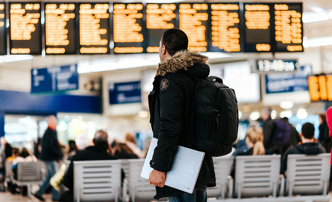 A man standing in an airport terminal looking at a large digital LED flight schedule board showing delays and cancellations due to airspace closures.