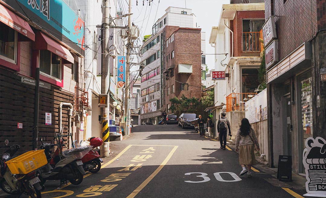 A quaint street in a Seoul neighbourhood showing traditional and modern Korean architecture under a clear sky.