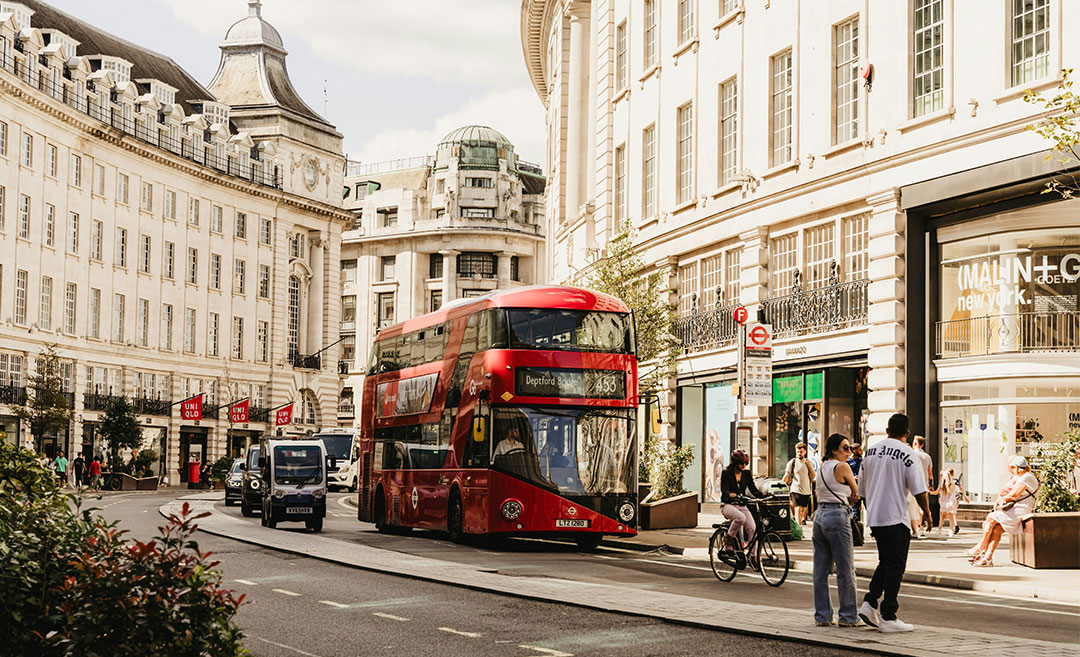 A classic red double-decker bus moving down a bustling city street in Europe, representing the transition from a holiday mindset to everyday life.