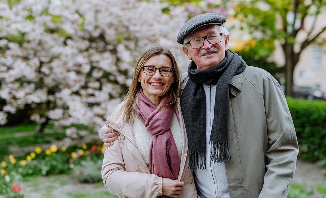 Adult daughter hugging her senior father outdoors in a park during a father daughter travel trip.