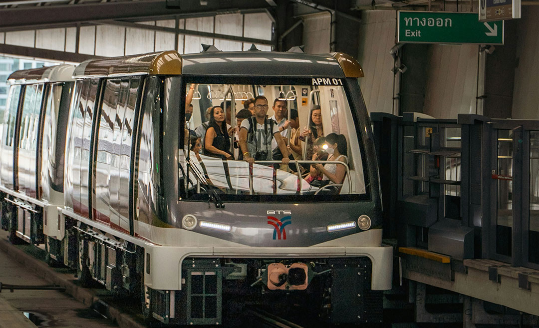 Exterior view from a station platform of a Bangkok BTS Skytrain with commuters standing inside the train carriage