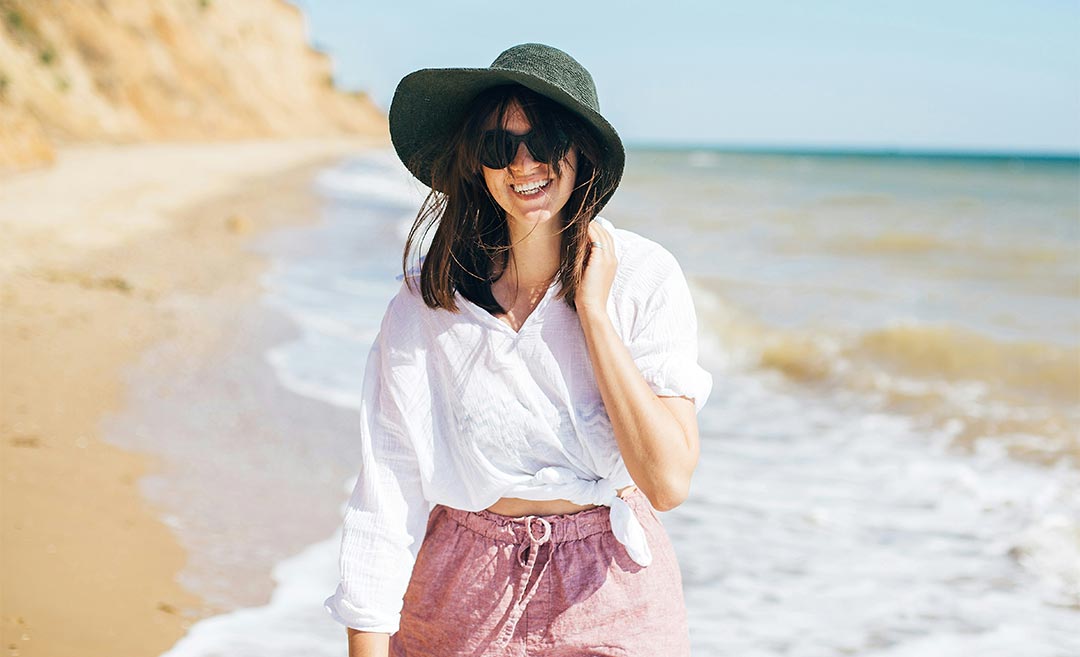 A woman walking along the shoreline in gentle tropical sea waves under a clear blue sky, illustrating the hope of rediscovering joy and warmth through travel.