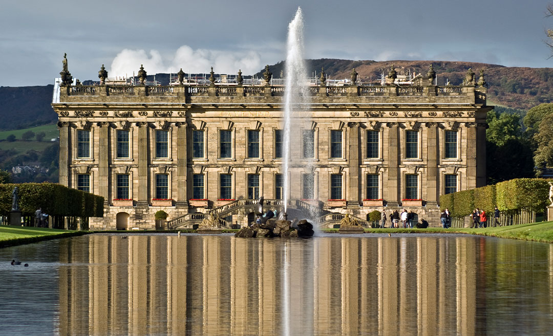The south front façade of Chatsworth House in Derbyshire, reflected in the lake with the Cascade and Emperor Fountain in the foreground