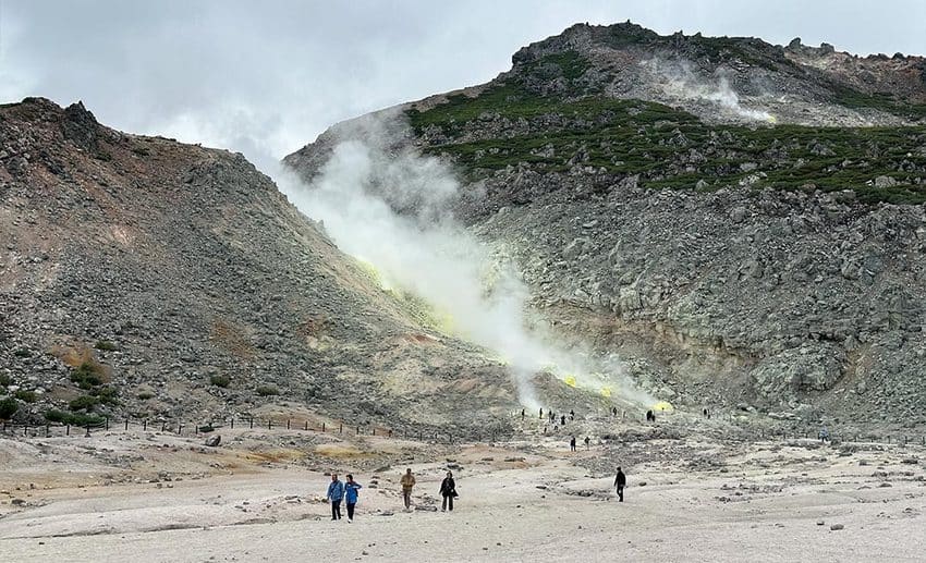 Hikers traversing volcanic terrain and wetlands along the East Hokkaido Trek in wilderness Japan.