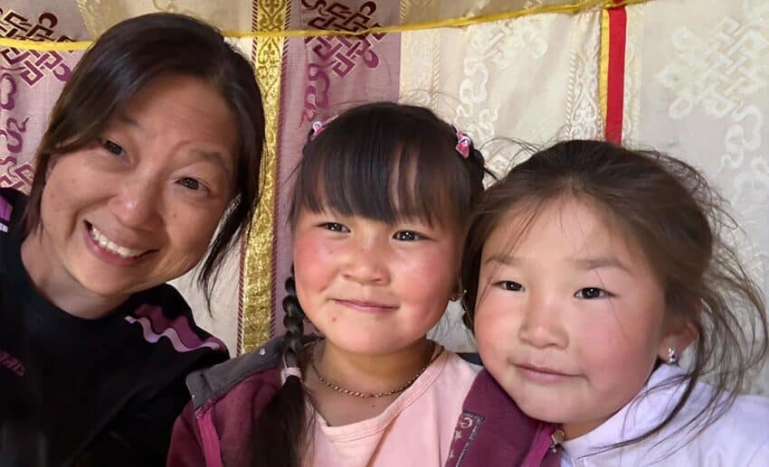 Selfie of Lynette Yee smiling together with two young Mongolian girls from her host family in the open countryside.